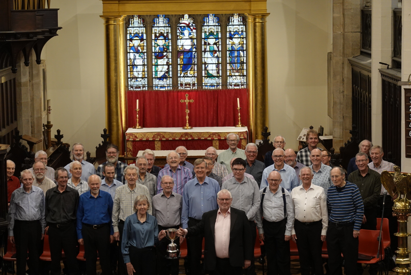 The Choir standing together on stage inside Huddersfield Parish Church. James and Jane are holding the trophy.