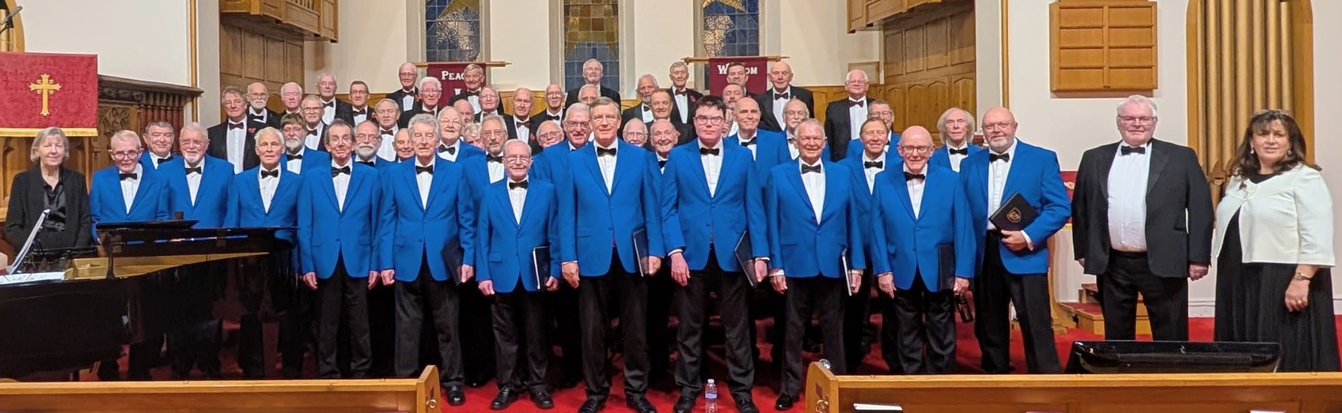 All members of Huddersfield Men's Voice stood together in their Blue blazers inside a church.