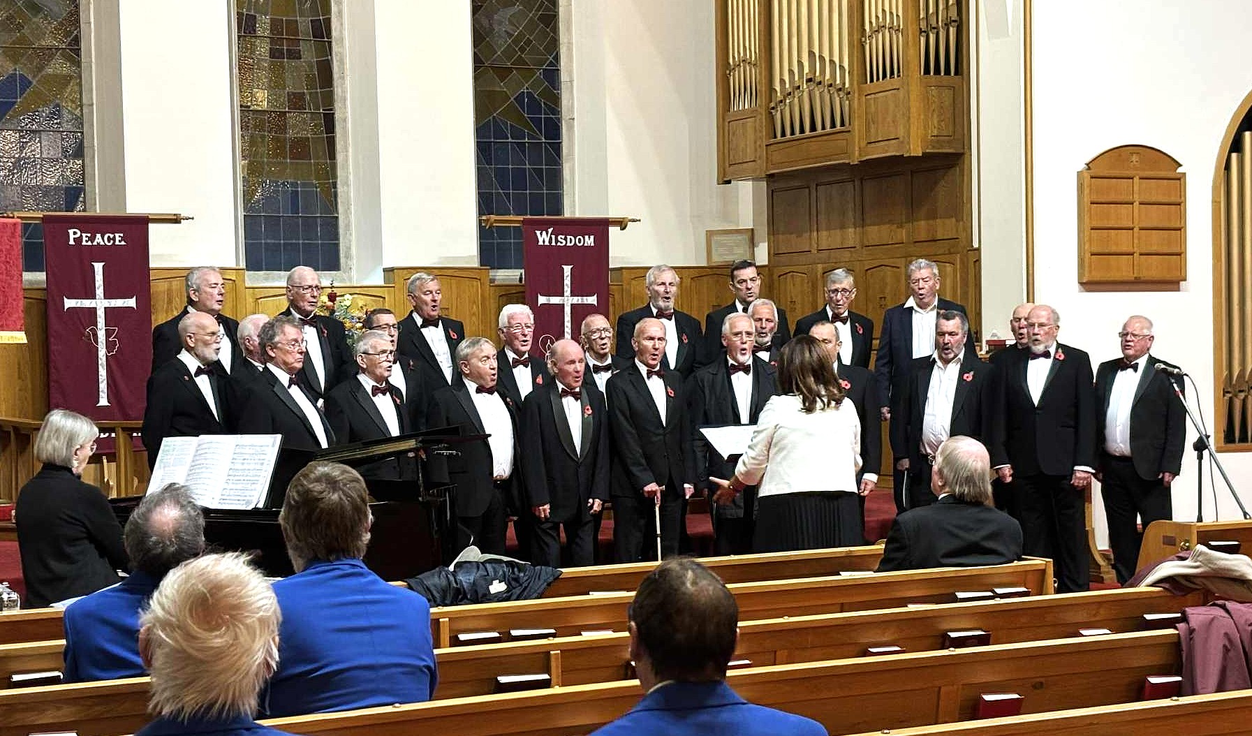 Cor Meibion Maelgwn Choir stood together in Black jackets and bow ties inside a church.