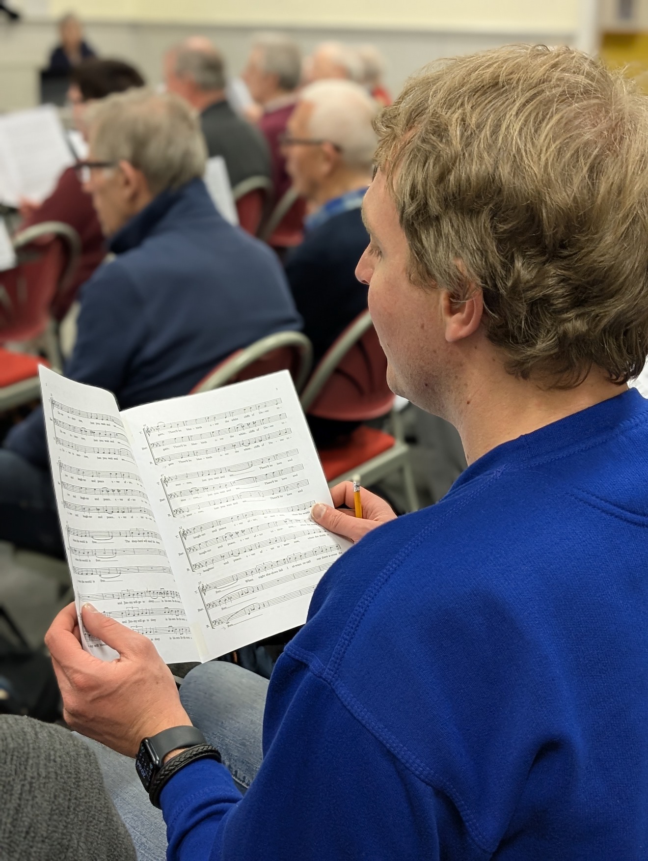 24:Choir rehearsal. Photo is a close up of choir members reading their music sheets.