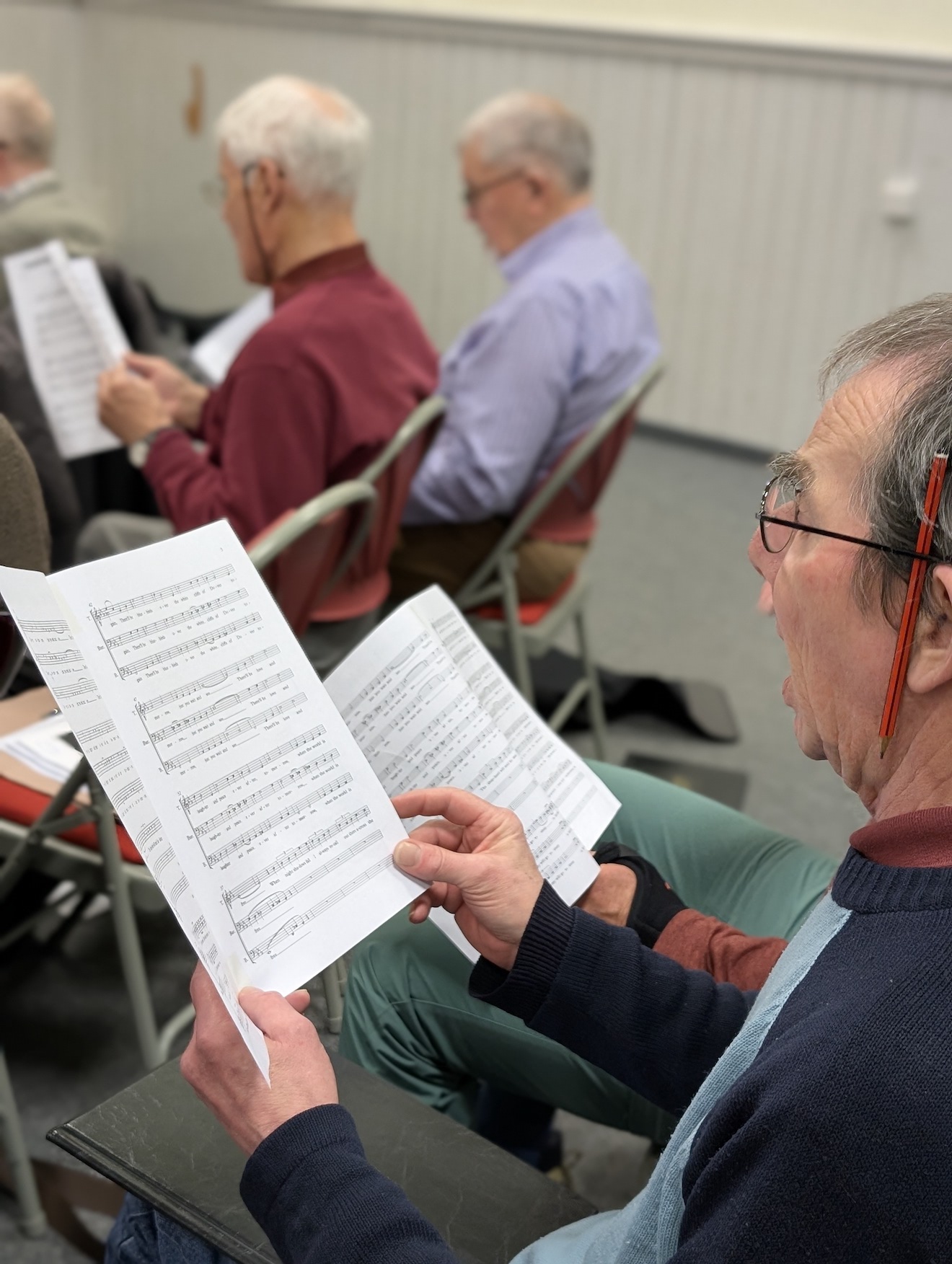 25:Choir rehearsal. Photo is a close up of choir members reading their music sheets.
